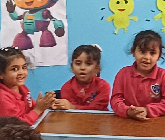 Drei ägyptische Kinder in roten Pullovern sitzen im Kindergarten an einem Tisch, die Wand im Hintergrund ist blau und hat fröhliche Bilder.