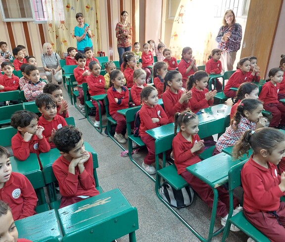 Ägyptische Kindergartenkinder sitzen an grünen Pulten im Unterricht. Dazwischen stehen ein paar ältere Frauen aus Österreich. 