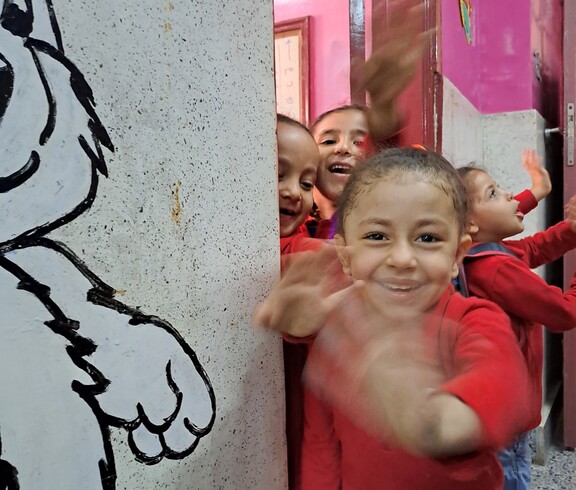 Ägyptische Kinder schauen aus der Tür zu ihrem Klassenzimmer und winken fröhlich in die Kamera.