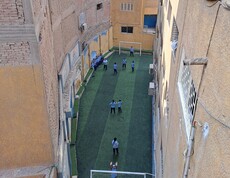 Blick von oben auf den Fußballplatz einer ägyptischen Grundschule, wo gerade Mädchen Fußball spielen. Der Platz ist zwischen hohen Häusern eingebettet.