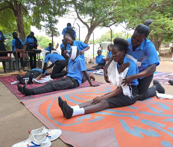 Junge Südsudanesinnen üben Verbandanlegen im Freien unter Bäumen. 