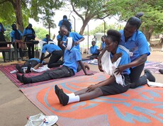 Junge Südsudanesinnen üben Verbandanlegen im Freien unter Bäumen. 